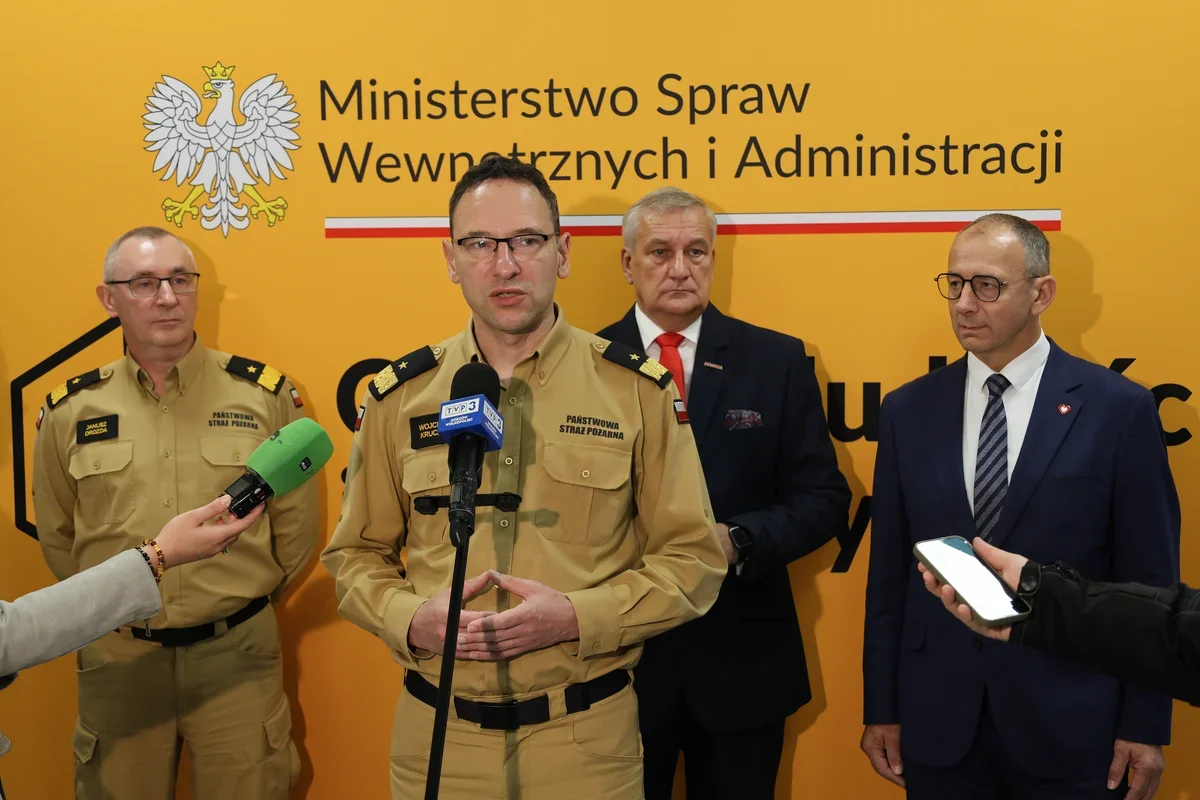 Przedstawiciel Państwowej Straży Pożarnej przemawia podczas konferencji prasowej przed ścianą z logotypem Ministerstwa Spraw Wewnętrznych i Administracji.