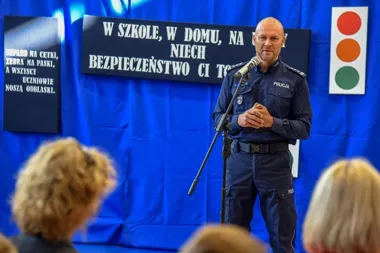 Policjant w mundurze przemawia do dzieci podczas szkolnej akcji bezpieczeństwa drogowego.