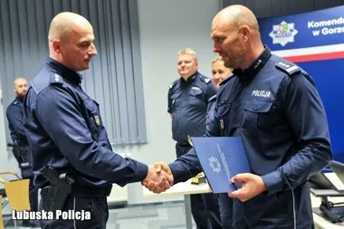 Funkcjonariusze policji w mundurach podczas uroczystego wręczenia dokumentu i uścisku dłoni w siedzibie Komendy w Gorzowie.