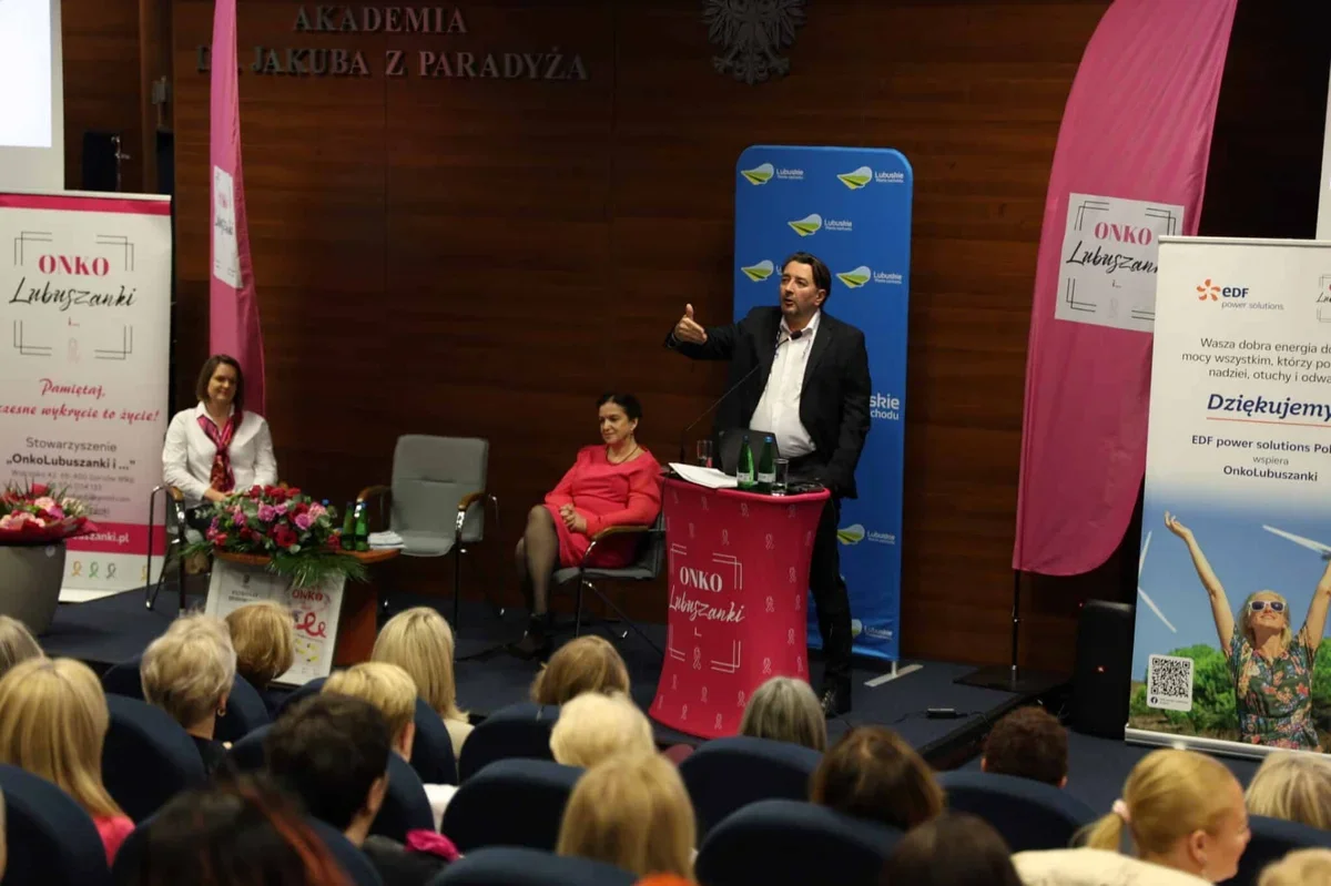 Mężczyzna w garniturze przemawia z czerwonego pulpitu podczas konferencji ONKO Lubuszanki w auli Akademii im. Jakuba z Paradyża, przed publicznością siedzącą na